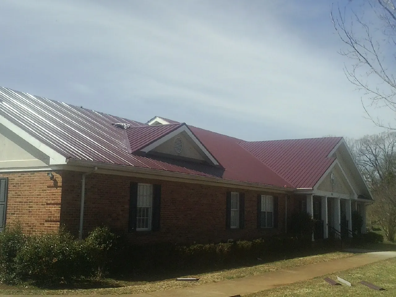 Red metal roof with gabled entries on a long brick building, from a Hail Damage Roof Repair job in Titusville
